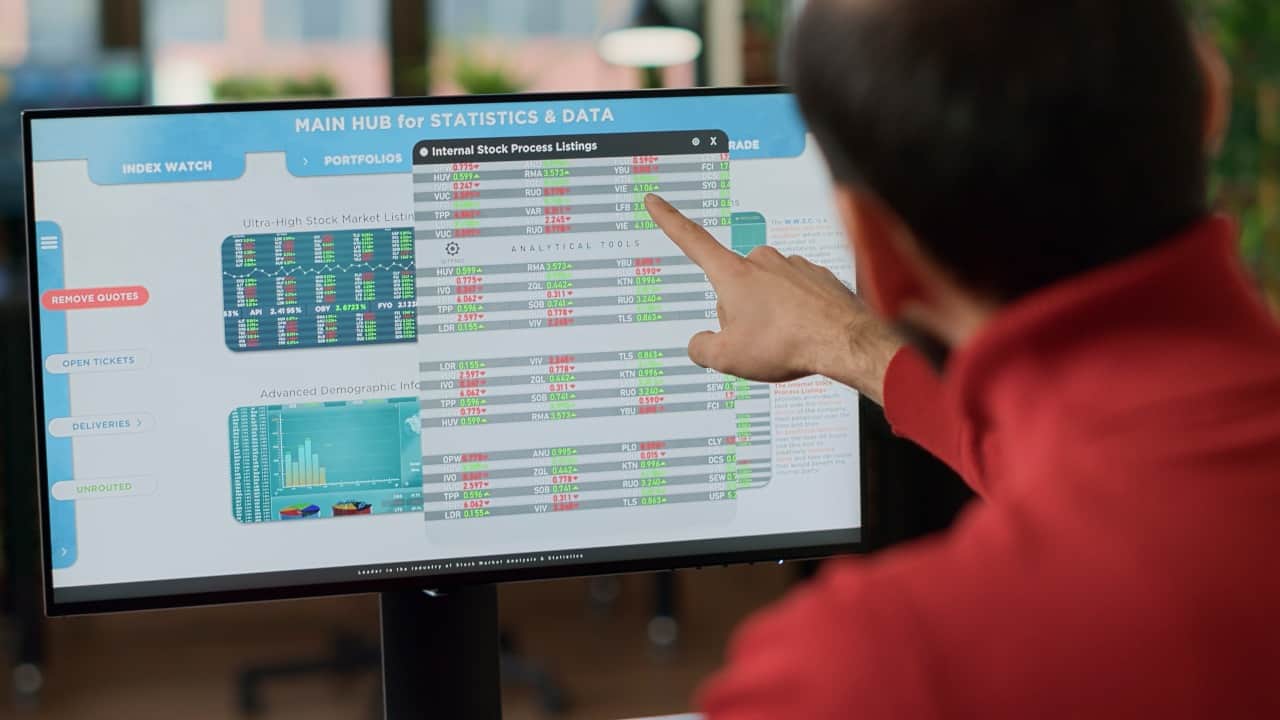 pointing at stock figures on monitor red turtleneck guy