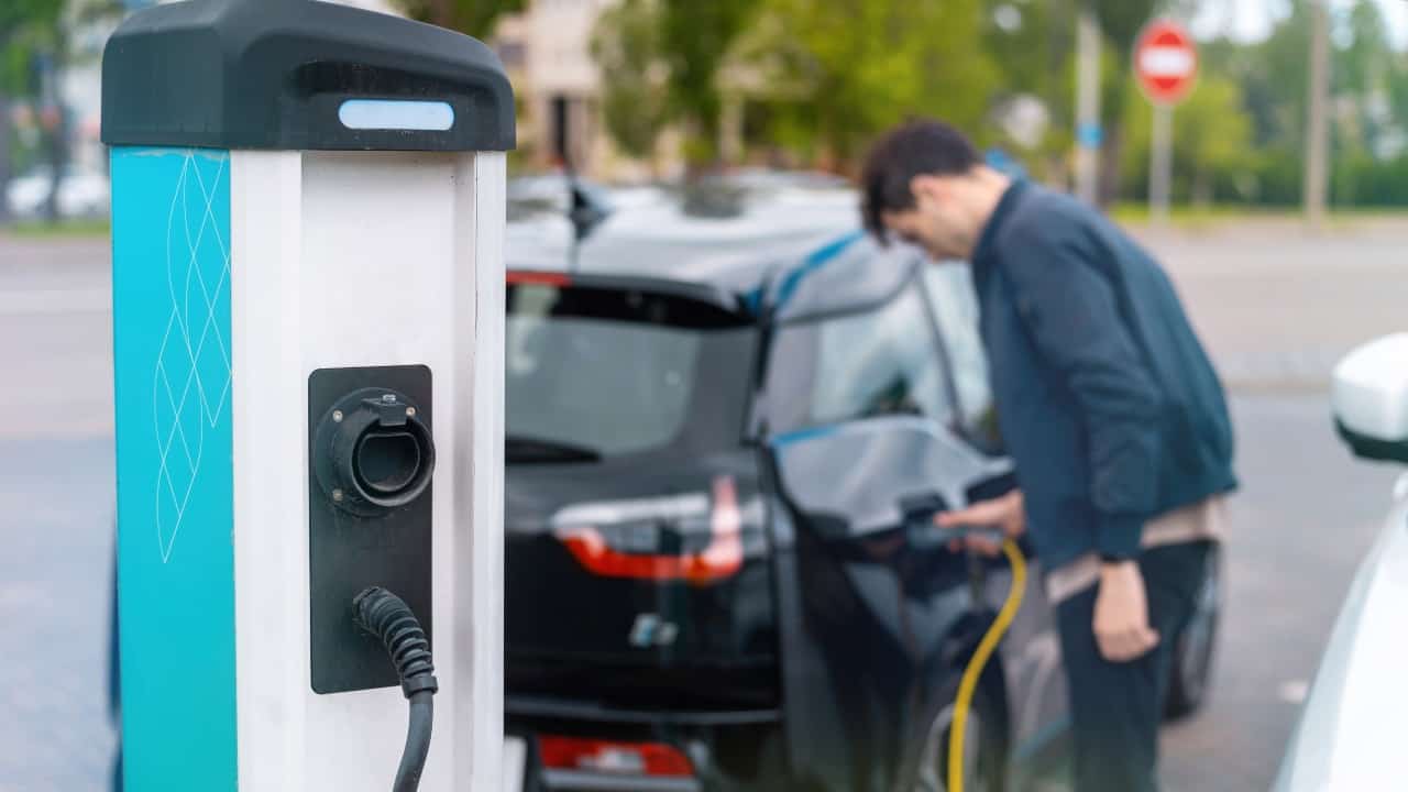 Man plugging in charger into an electric car at charge station