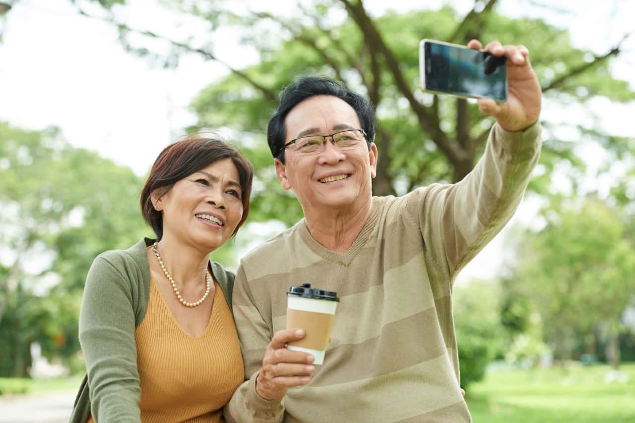 Joyful Vietnamese senior couple taking selfie in park